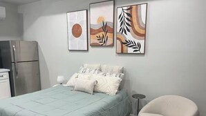 Une chambre à coucher avec un lit, une chaise et des œuvres d’art accrochées au mur.