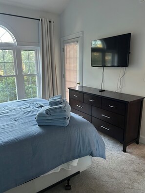 Quarto com cama, cômoda, televisão e janela com cortinas.