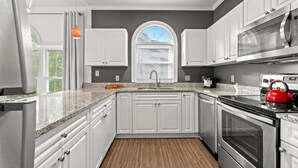 A modern kitchen with white cabinets, granite countertops, a stainless steel oven, and a red kettle. - Bright 2 BR, Fully Equipt, 3rd Floor Cozy Condo in Myrtle Beach (Myrtle Beach)