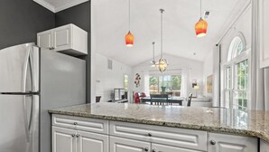 A kitchen with white cabinets, a stainless steel refrigerator, granite countertops, pendant lights, and a dining area with a table and chairs. - Bright 2 BR, Fully Equipt, 3rd Floor Cozy Condo in Myrtle Beach (Myrtle Beach)