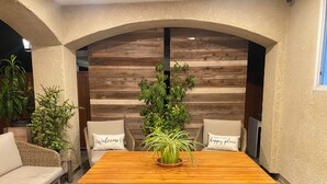 Un rincón comedor acogedor con una mesa de madera y bancos, rodeado de muebles de mimbre y plantas en macetas.