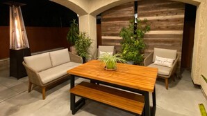 Un rincón al aire libre acogedor con una mesa de madera, sofás con cojines y una planta en maceta.