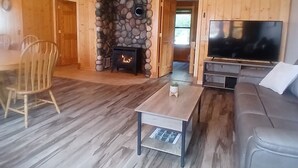 L’intérieur chaleureux d’un chalet avec une cheminée en pierre, un téléviseur, un canapé et un coin repas avec des chaises.