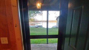 Une porte donnant sur un espace pavé où se trouvent un banc, un lampadaire, et d’où l’on peut admirer un plan d’eau et des bateaux.
