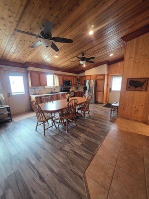 A spacious kitchen with wooden cabinets, a dining table with chairs, and a ceiling fan.