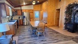 Un intérieur en bois comprenant une table à manger, des chaises, un banc, un réfrigérateur, une cuisinière et un mur en pierre.