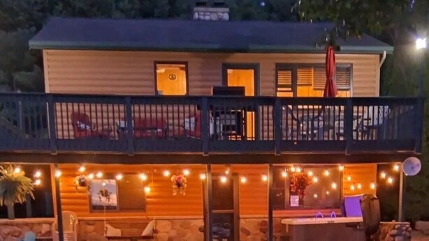 Une maison à deux étages avec un balcon, des fondations en pierre et des guirlandes lumineuses.