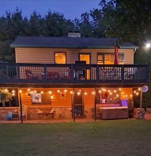 A two-story house with a balcony, stone foundation, and string lights.