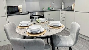 Une cuisine moderne avec des meubles blancs, une table de salle à manger ronde entourée de quatre chaises et un four à micro-ondes encastré.