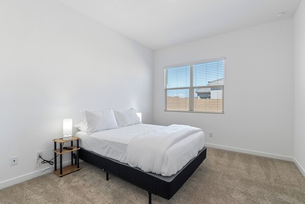 A bedroom with a bed, a bedside table, a lamp, and a window. - Quiet Quarter in Laveen Village (Laveen)