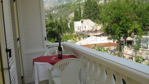 Un balcón con una mesa y una silla, con vistas a un paisaje montañoso con árboles y un edificio.