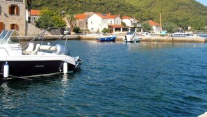 Un port de plaisance avec des bateaux amarrés, un bâtiment en pierre et des maisons aux toits rouges.