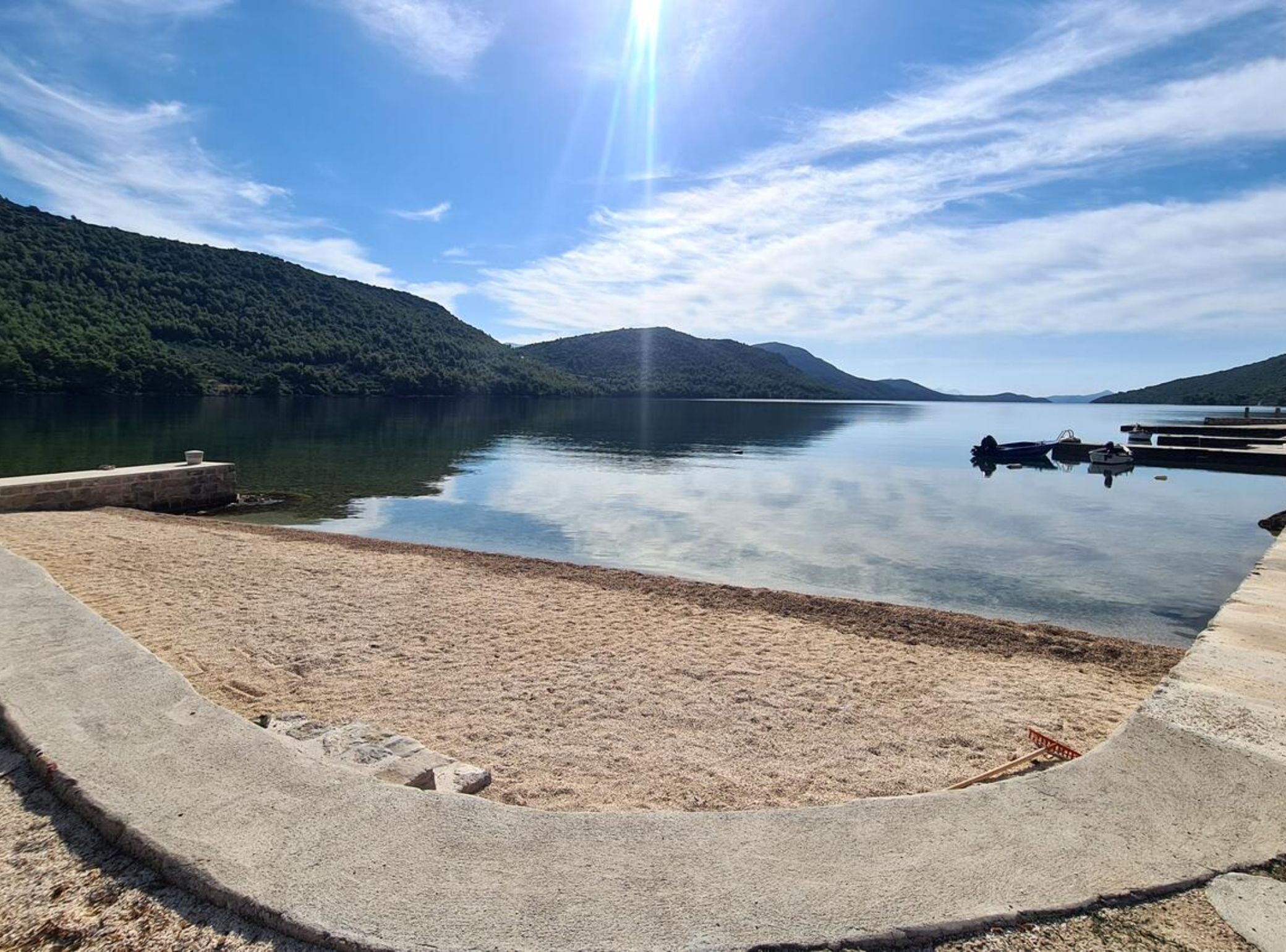 A calm lake with a dock and boats, surrounded by forested hills.