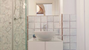 Ein Badezimmer mit Duschkabine aus Glas, einem weißen Waschbecken und einem gefliesten Boden.