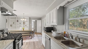 Una cucina moderna con mobili bianchi, un lavello in acciaio inossidabile e un'area pranzo con tavolo e sedie.