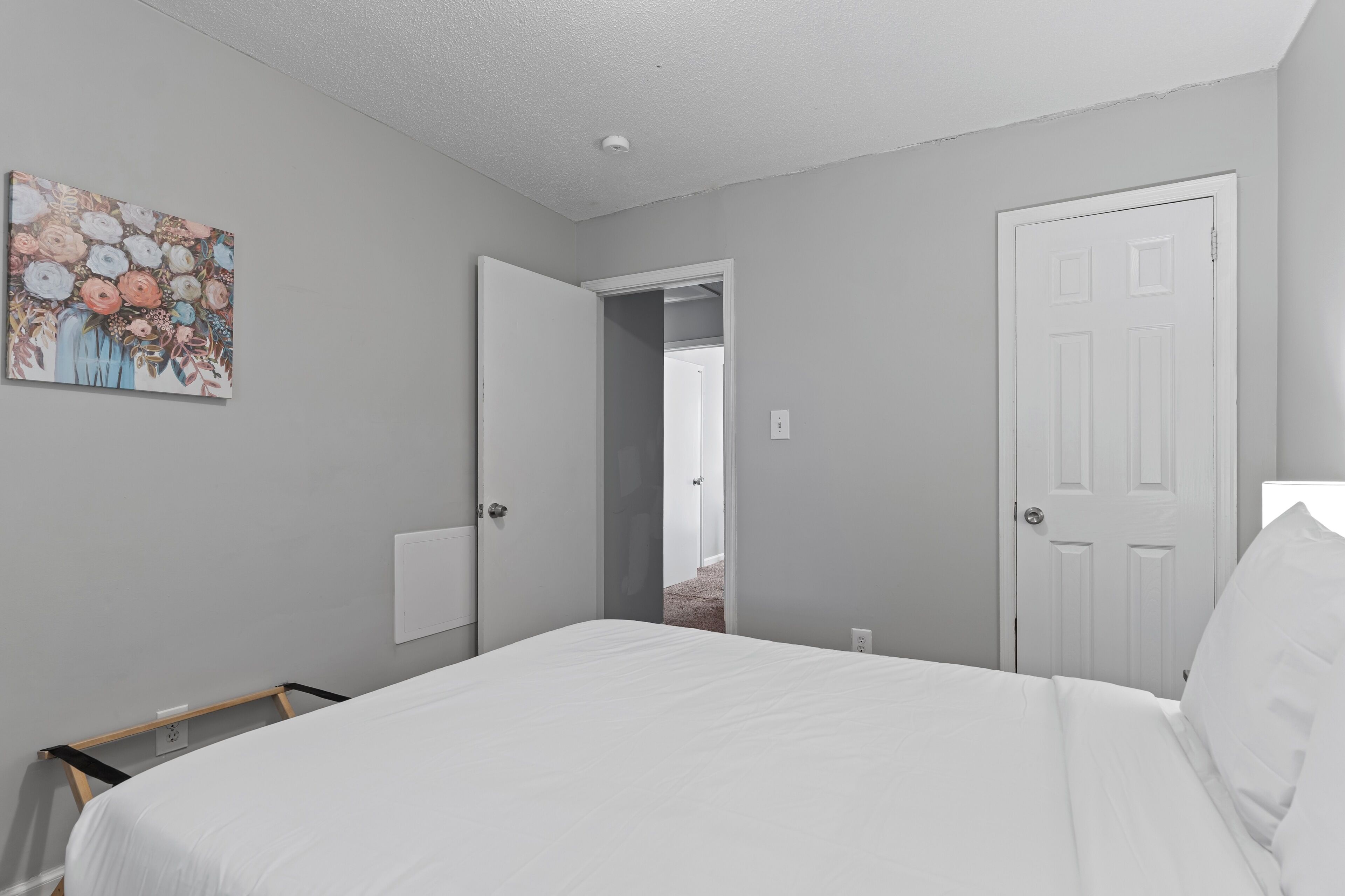 A bedroom with a bed, a door, a closet, and a painting on the wall.