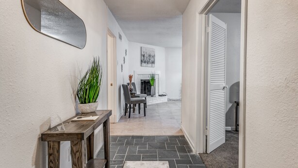 A hallway with a wooden console table, a potted plant, a mirror, and a fireplace in the background. - Near Parks Tranquil Fox Trails (Memphis)