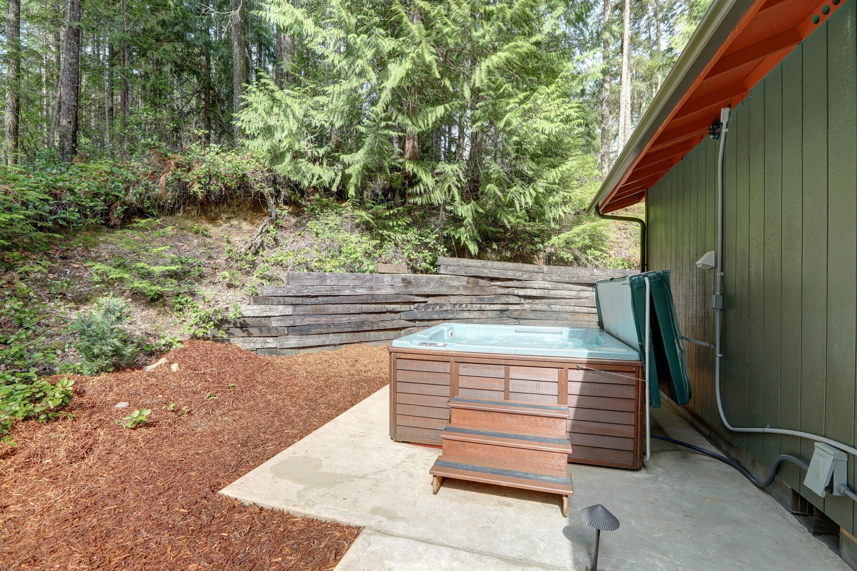 Un bain à remous dans un jardin, avec une terrasse en bois et un mur en pierre.