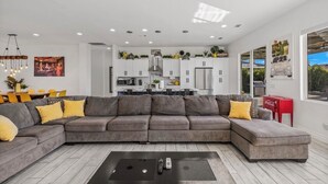 A modern living room with a grey sectional sofa, a coffee table, and a dining area with yellow chairs.