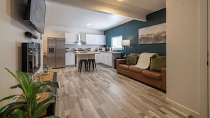 A modern kitchen with white cabinets, a stainless steel refrigerator, and a flat-screen TV mounted on the wall. - Downtown Garden Escape (Casper)