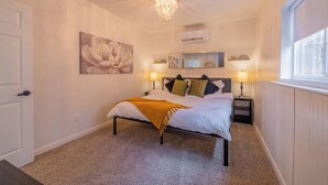 A bedroom with a bed, bedside lamps, a chandelier, a large floral painting, a mirror, and a window. - Downtown Garden Escape (Casper)