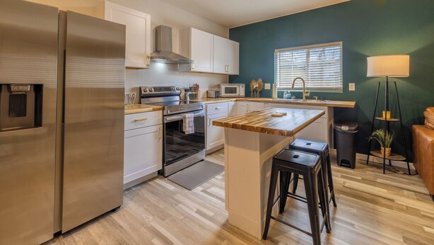 A modern kitchen with stainless steel appliances, white cabinetry, and a wooden island with stools. - Downtown Garden Escape (Casper)