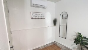 A hallway with a white wall, a brown rug, a potted plant, and a mirror. - Downtown Garden Escape (Casper)