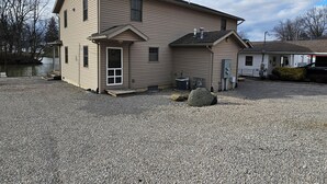 Una casa a due piani con un portico, un piccolo garage annesso e un vialetto sterrato.