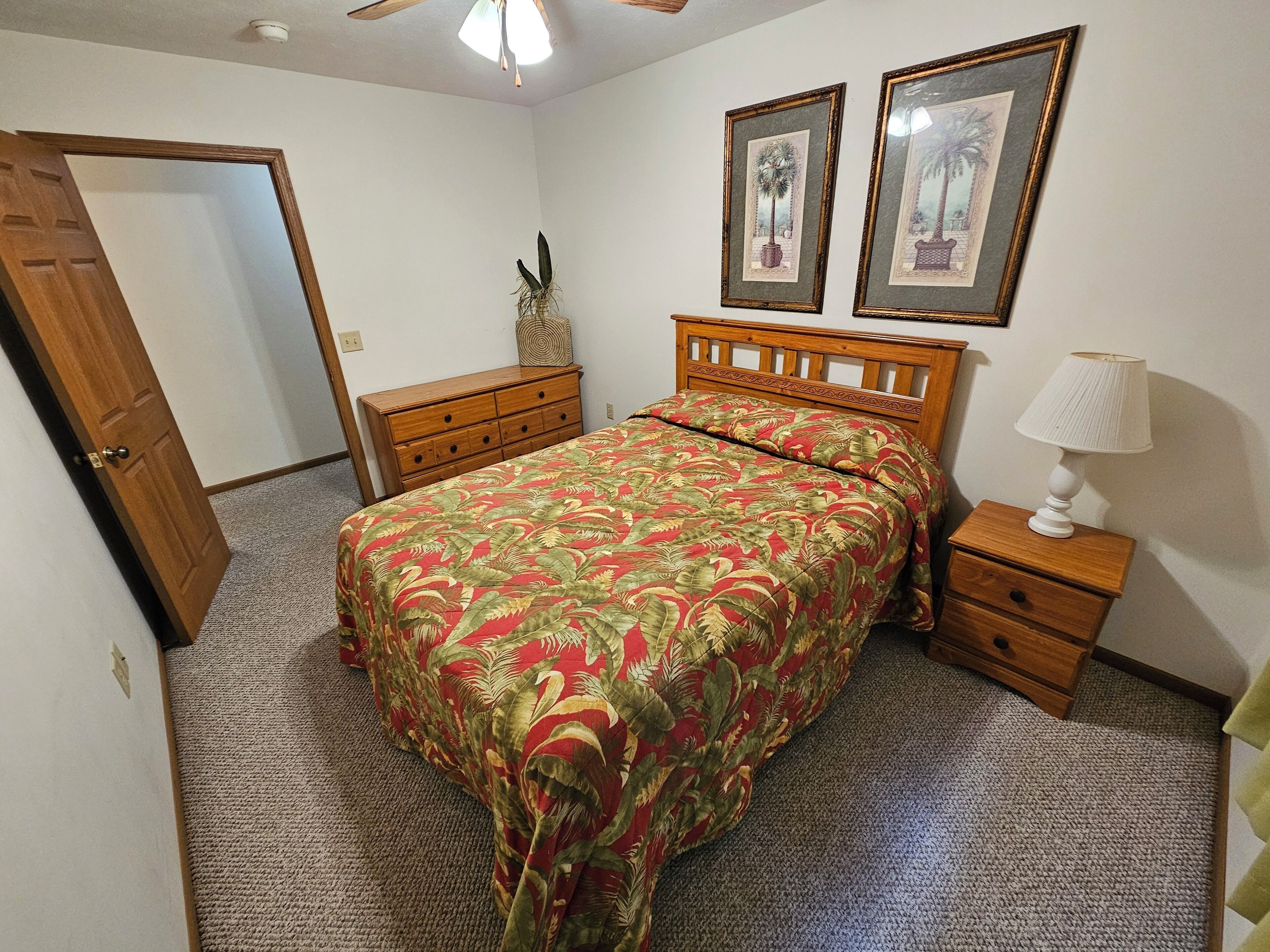 A bedroom with a bed, a nightstand, a dresser, and two framed pictures on the wall.