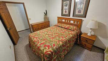 A bedroom with a bed, a nightstand, a dresser, and two framed pictures on the wall.