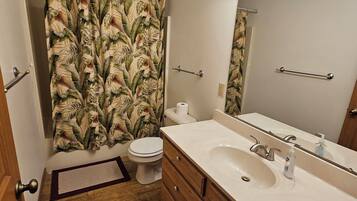 A bathroom with a shower curtain, toilet, sink, and mirror.