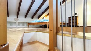 A spacious room with a high ceiling, wooden beams, a bed with a blue cover, and a small table. - Casa Marta - Affitti Brevi Italia (Lecco)