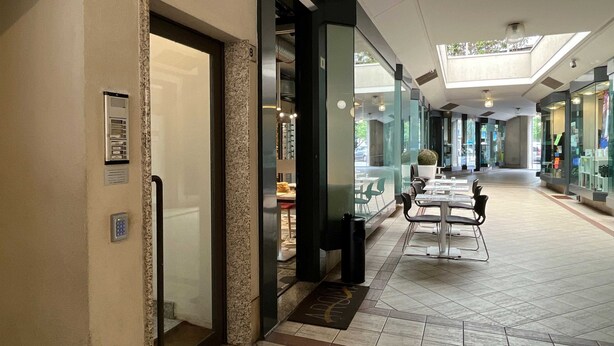 A corridor with a glass storefront on the left, a reception desk, and a seating area with tables and chairs. - Casa Marta - Affitti Brevi Italia (Lecco)