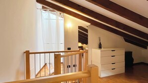 A loft bedroom with a wooden staircase, a white dresser, and a small table with a vase. - Casa Marta - Affitti Brevi Italia (Lecco)