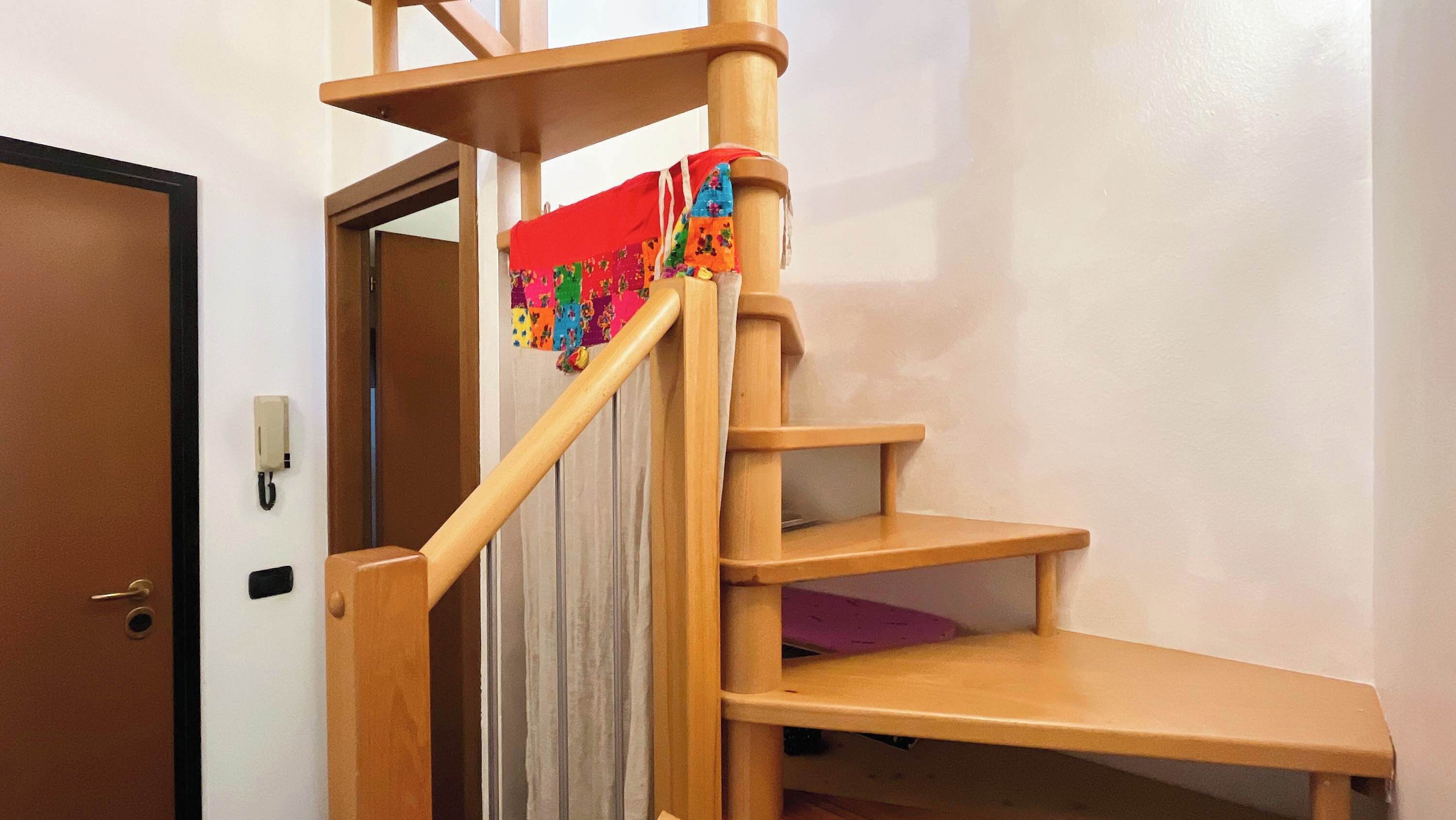 A wooden spiral staircase with a red cloth covering the handrail.