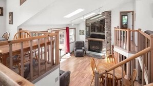 A spacious living area with a high ceiling, a stone fireplace, wooden furniture, and a staircase leading to an upper level. - 5-Bedroom Lakefront, private beach wifi AC boat & kayaks near ski, casino (Tobyhanna)