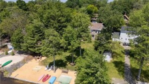 A lakeside property with a dock, boats, and a house surrounded by dense trees. - 5-Bedroom Lakefront, private beach wifi AC boat & kayaks near ski, casino (Tobyhanna)