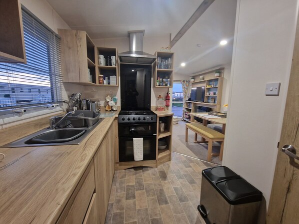 A compact kitchen with wooden cabinets, a stove, and a sink. - Remarkable 3-bed Lodge in Tattershall (Lincoln)
