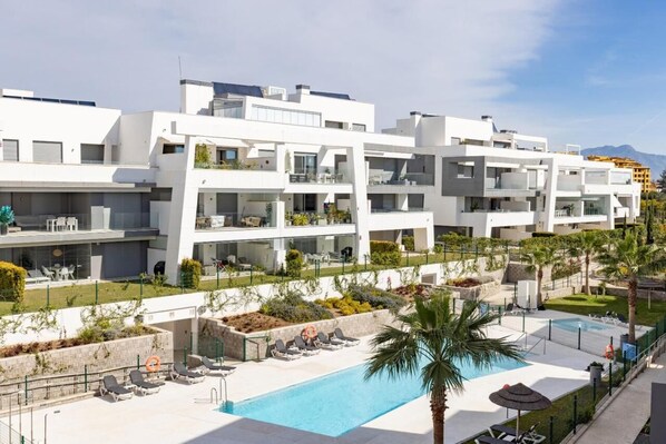 A modern hotel with multiple balconies, a swimming pool, and a landscaped garden.