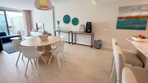 A modern living room with a round dining table, white chairs, a sofa, and a large window. - Exclusive penthouse with 2 bedrooms and sea views  (Estepona)