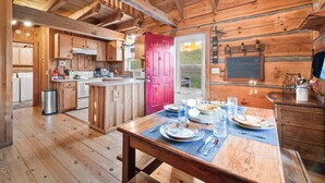 A wooden cabin interior with a kitchen, dining area, and a red door. - Gorgeous Cabin - Fast 100mbps WiFi - Pet Friendly! (Meadows of Dan)
