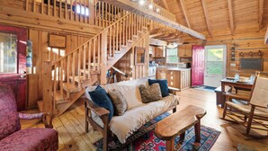A wooden cabin interior with a staircase, a sofa, a rocking chair, and a kitchen area. - Gorgeous Cabin - Fast 100mbps WiFi - Pet Friendly! (Meadows of Dan)