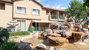 A building with a water feature in front, including a small waterfall and rocks. - Fully Furnished Remodeled Condo 2 Bed 2 Bath Superstition Springs on 1 level  (Mesa)