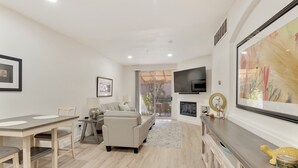 A modern living room with a dining area, a sofa, a TV mounted on the wall, and a fireplace. - Fully Furnished Remodeled Condo 2 Bed 2 Bath Superstition Springs on 1 level  (Mesa)