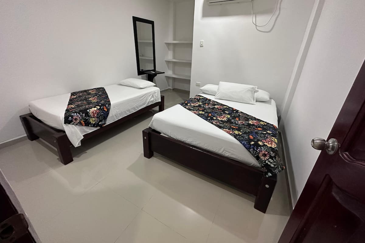 A room with two single beds, a mirror, an air conditioning unit, and a door.