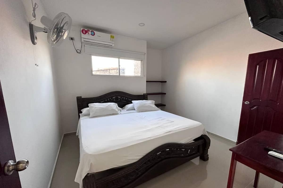 A bedroom with a bed, a wall-mounted air conditioner, a window, and a door.