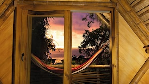 A cozy room with a wooden ceiling, a hammock, a wooden table with a plant, and a patterned rug.