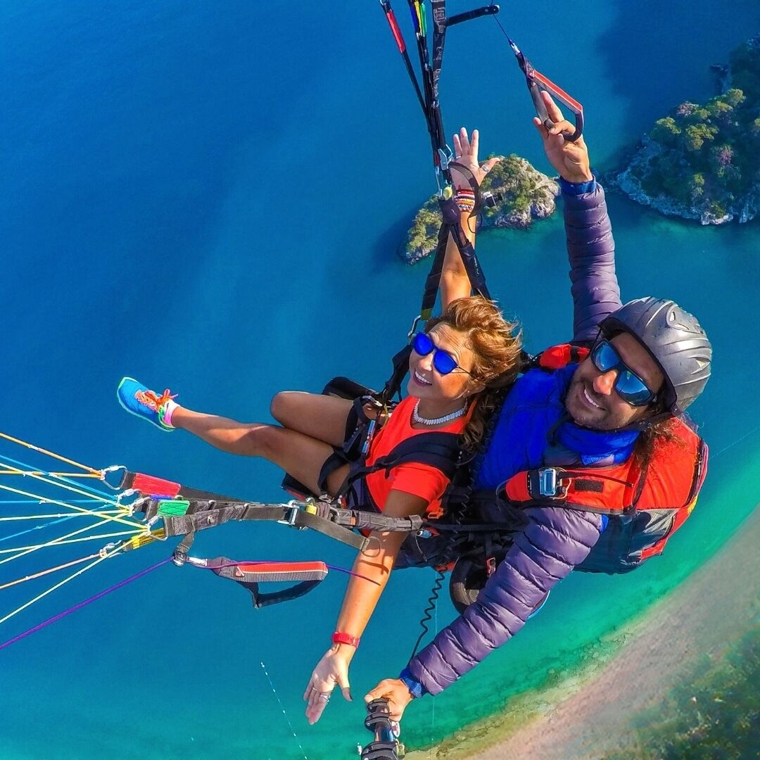 Una persona che pratica parapendio sopra una zona costiera con acque blu cristalline e isole in lontananza.