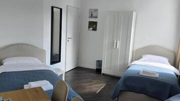 Una habitación de hotel con dos camas, una mesa de madera y un armario.