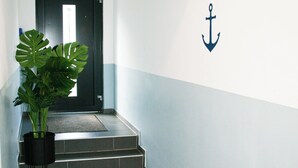 A hallway with a potted plant, a carpeted area, and a door with an emergency exit sign. - Hotel am Seehafen (Hamburg)